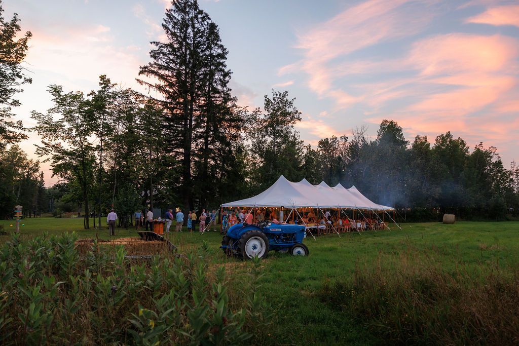 A blue tractor is parked in a field with a tent in the background.