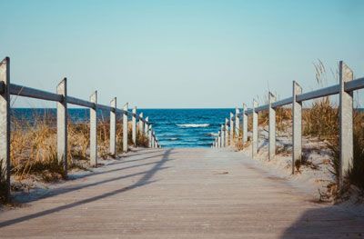 A wooden walkway leading to the ocean with a fence.