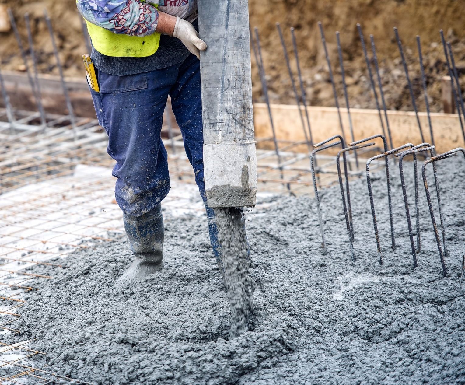 Construction workers pouring and leveling concrete on a road with orange safety cones.