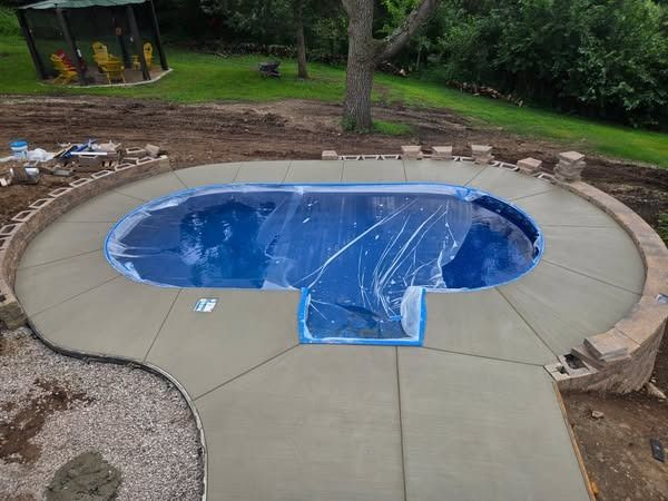 Pool construction: concrete patio surrounding covered pool in a grassy backyard.