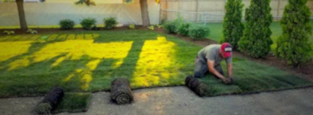 Yellow riding lawnmower on striped green grass, cutting a lawn in front of a building.