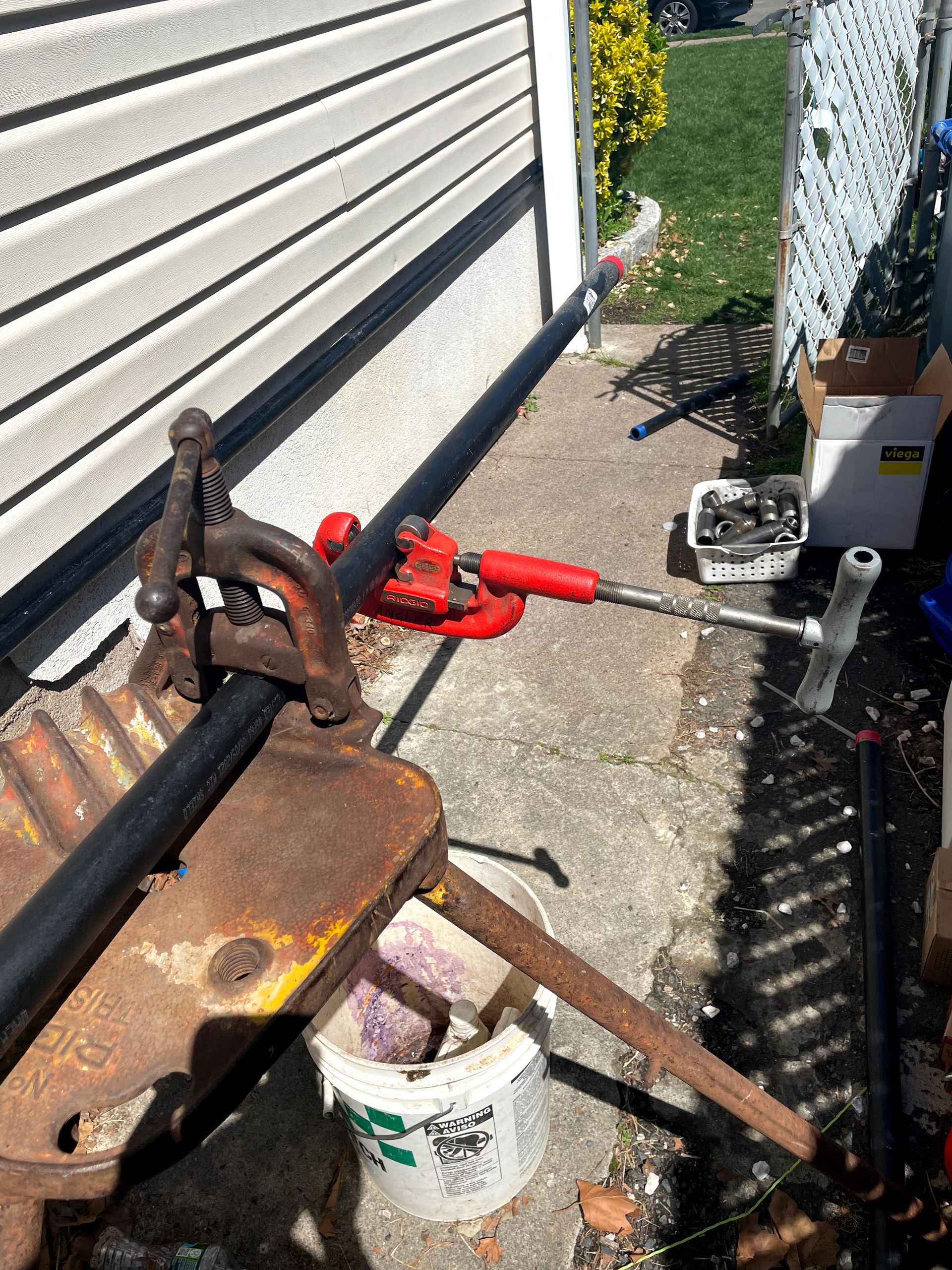 A pipe clamp is sitting on the sidewalk next to a bucket.