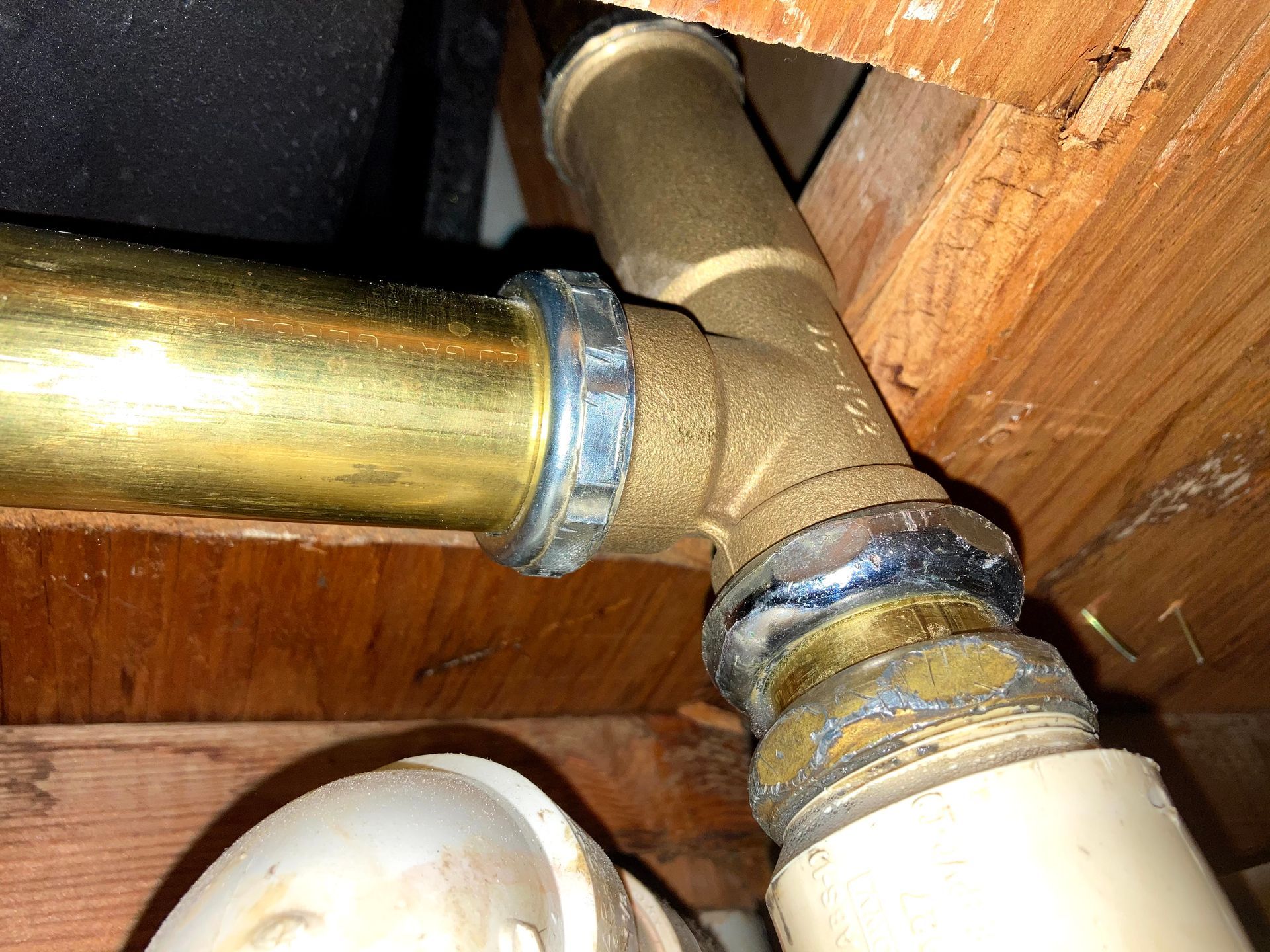 A brass pipe is connected to a white pipe under a wooden ceiling.