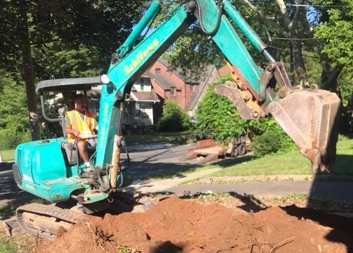 A man is driving an excavator in a driveway.
