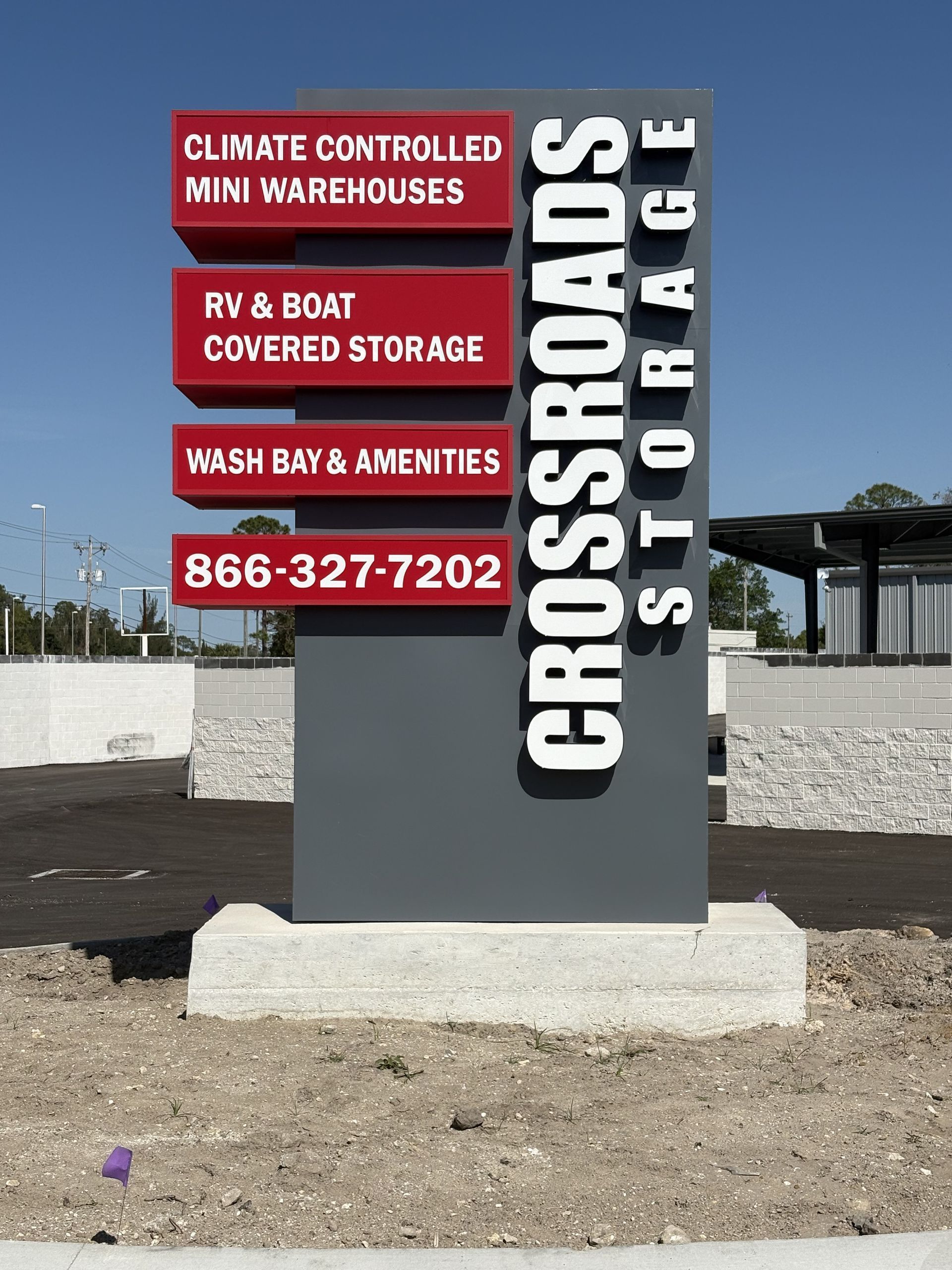 A gray Crossroads Storage monument sign with red panels listing services and a phone number against a clear blue sky.