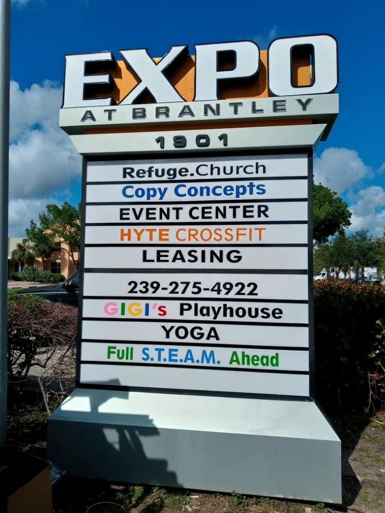 A sign for Expo at Brantley listing businesses, including a church, crossfit gym, and Gigi's Playhouse against a blue sky.