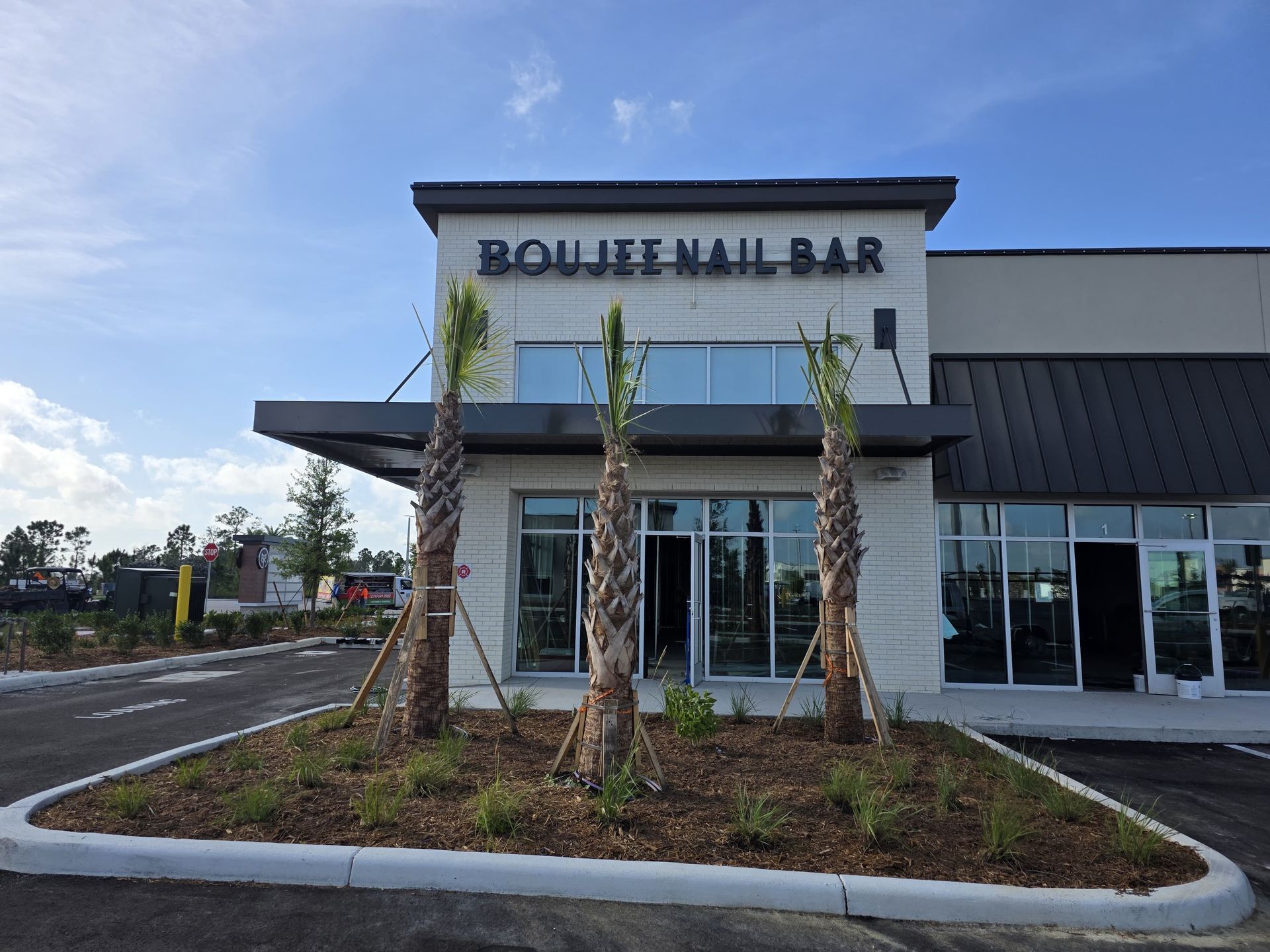Boujee Nail Bar storefront in a modern strip mall with three young palm trees in a garden bed in front.