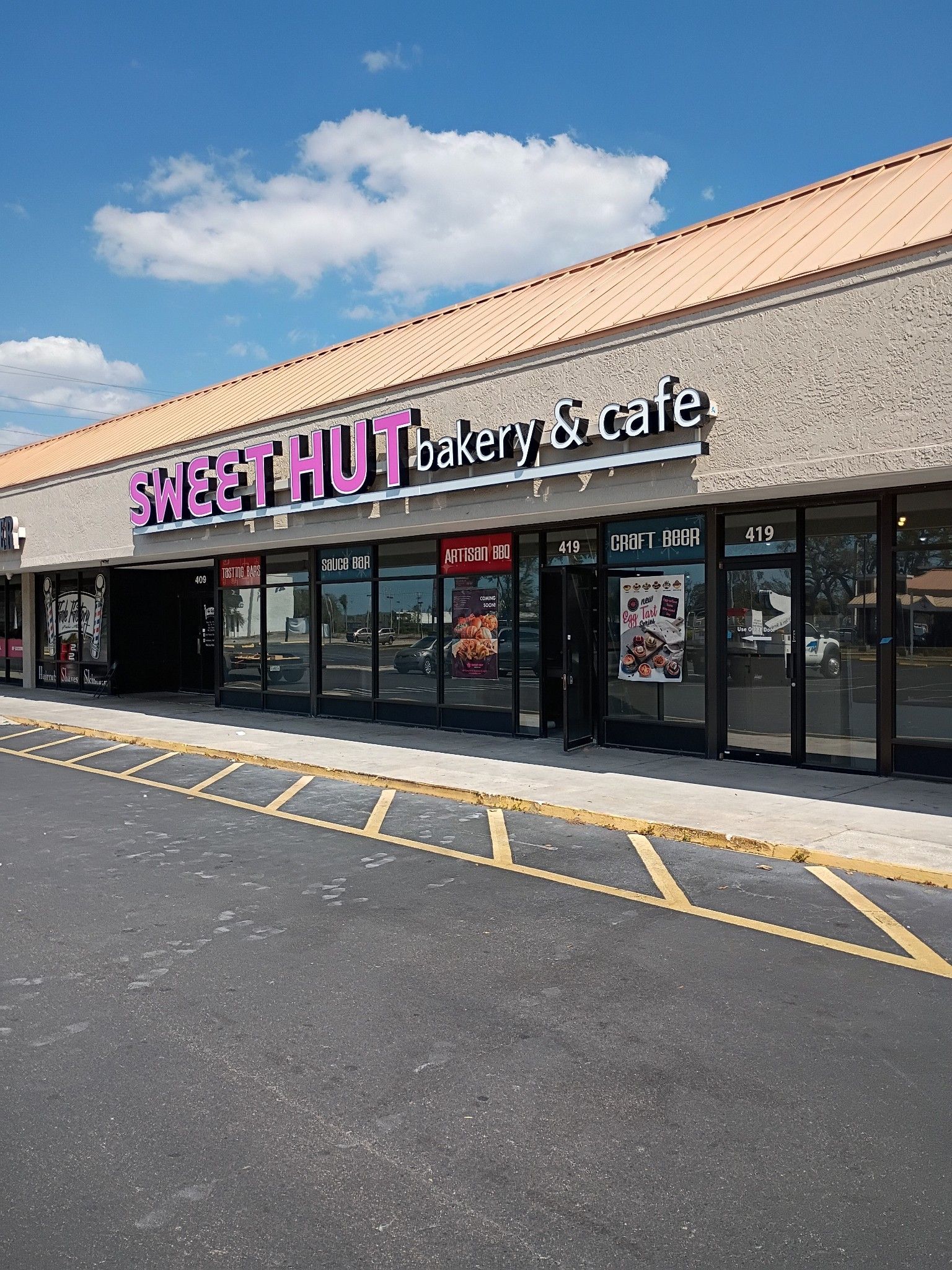 A Sweet Hut Bakery & Cafe storefront with purple signage in a strip mall parking lot under a clear blue sky.