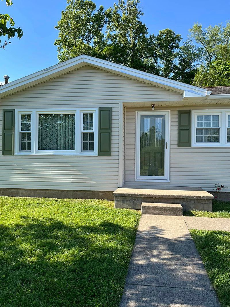 A small white house with green shutters and a walkway leading to it.
