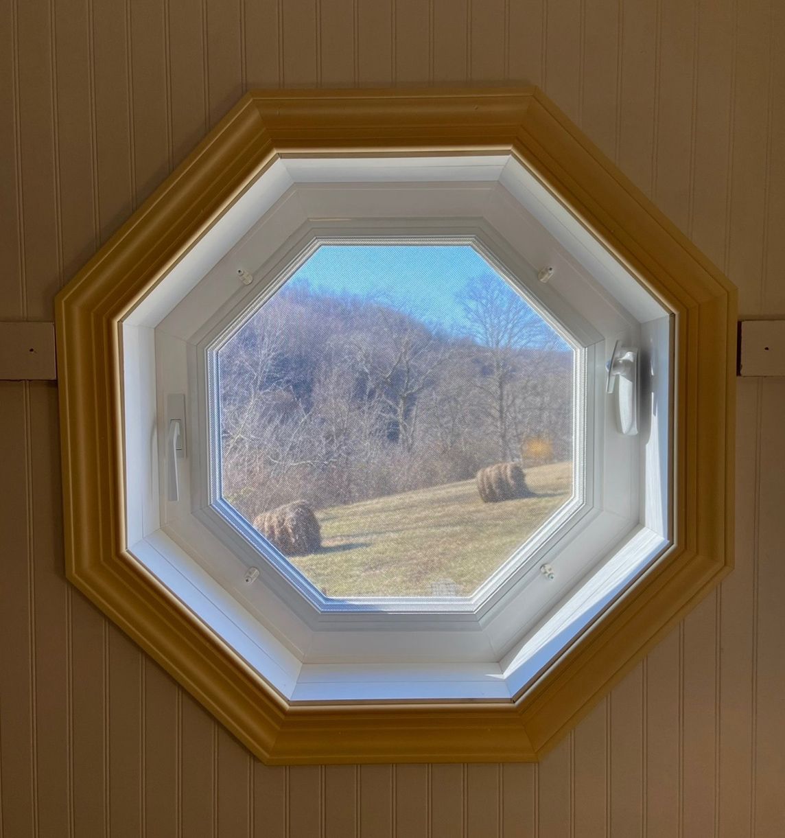 An octagonal window with a view of a field of hay bales
