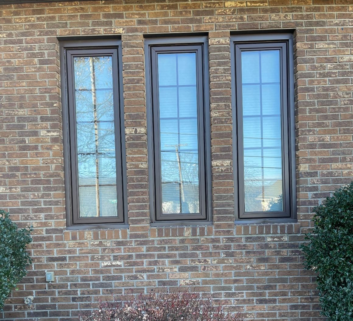 Three windows are on a brick wall of a house.