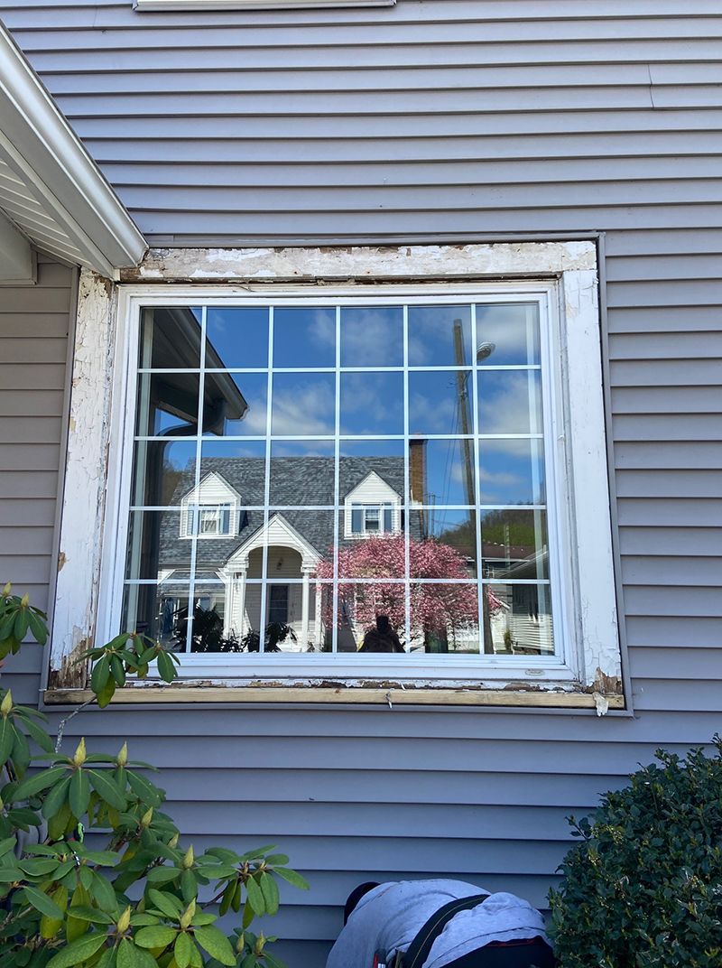A man is painting a window on the side of a house.