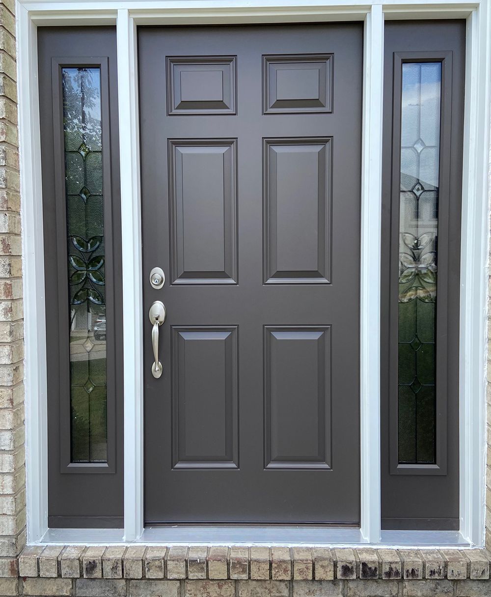 A brown front door with two side windows on a brick building.