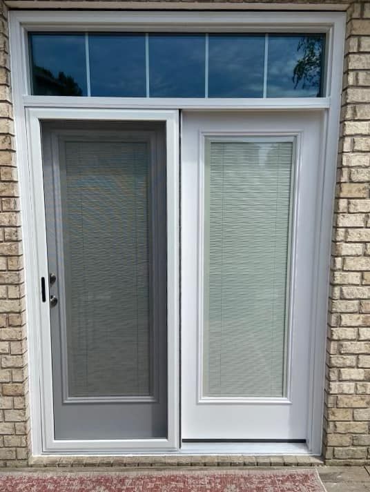 A white sliding glass door with blinds on it is on a brick wall.