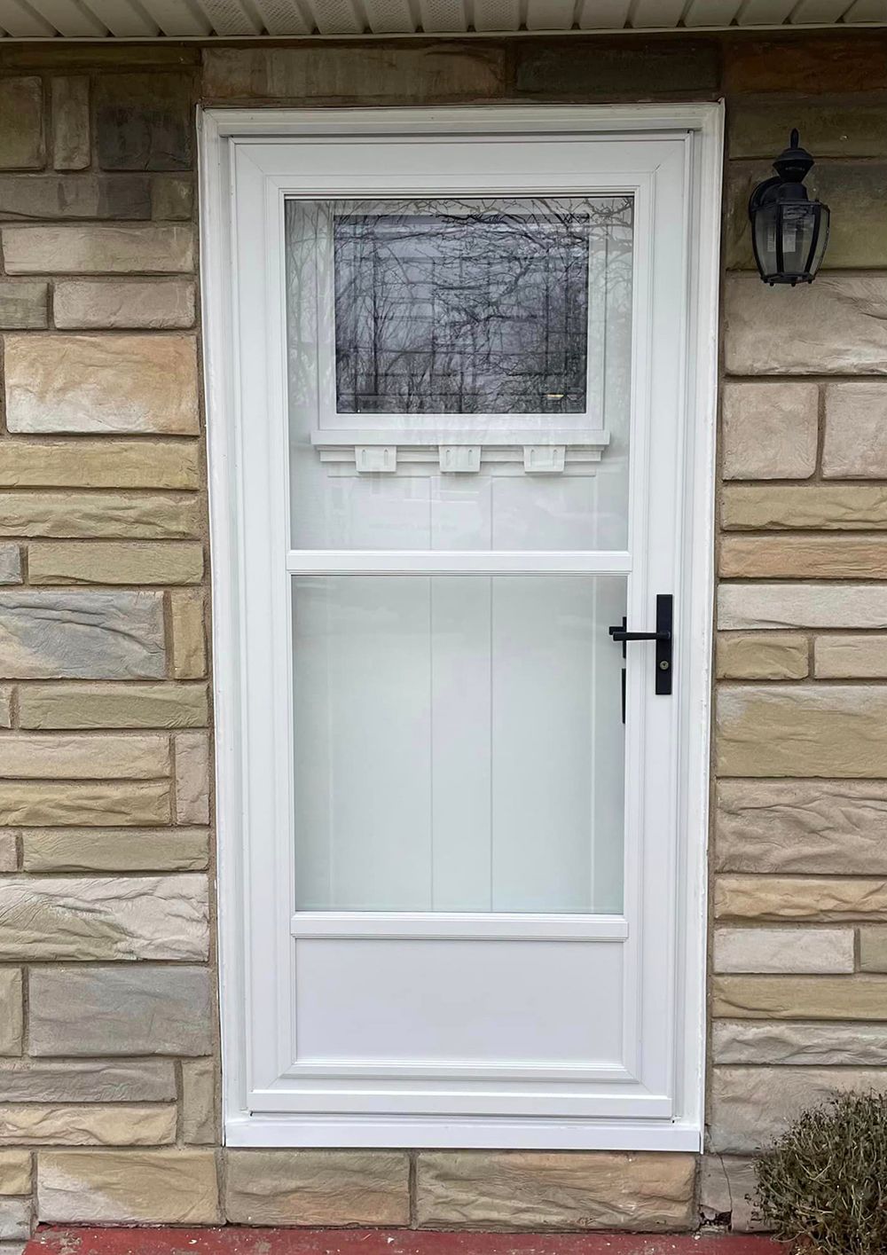 A white screen door is on a brick wall.