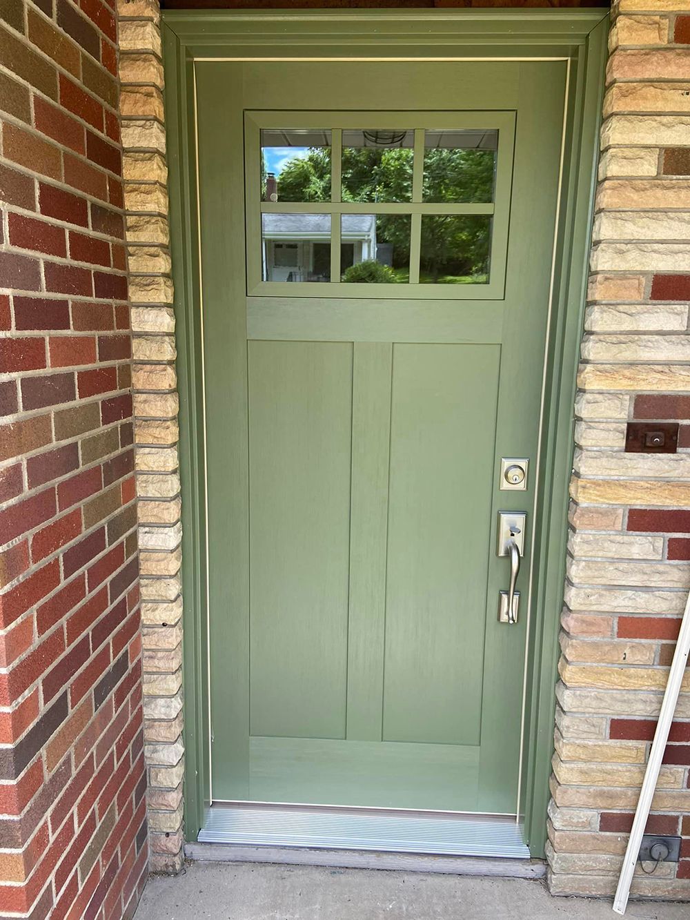 A green door is sitting in front of a brick wall.