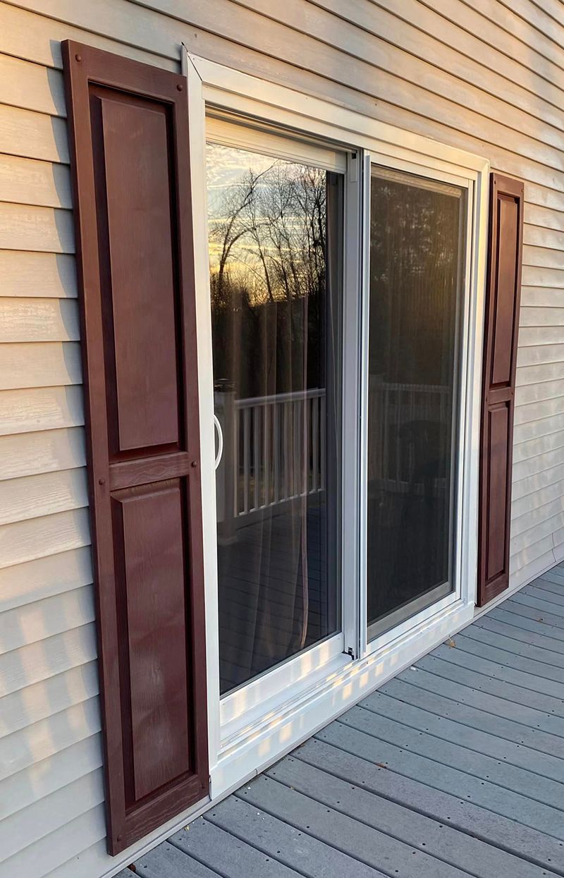 A sliding glass door with brown shutters on a house.