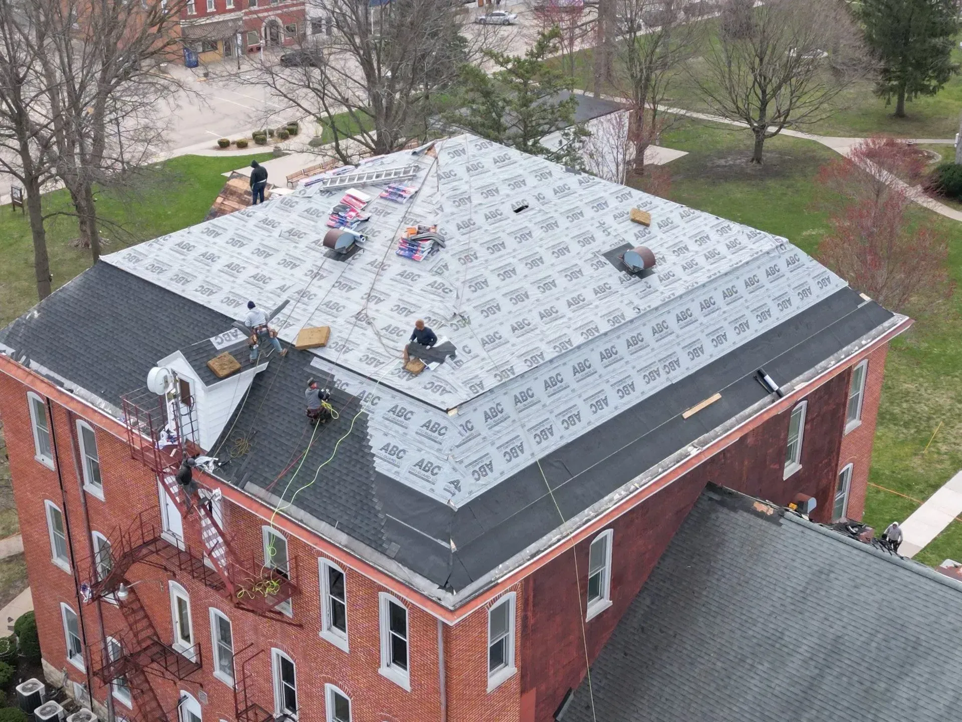 Aerial view of a brick building roof under repair with workers and roofing materials on top