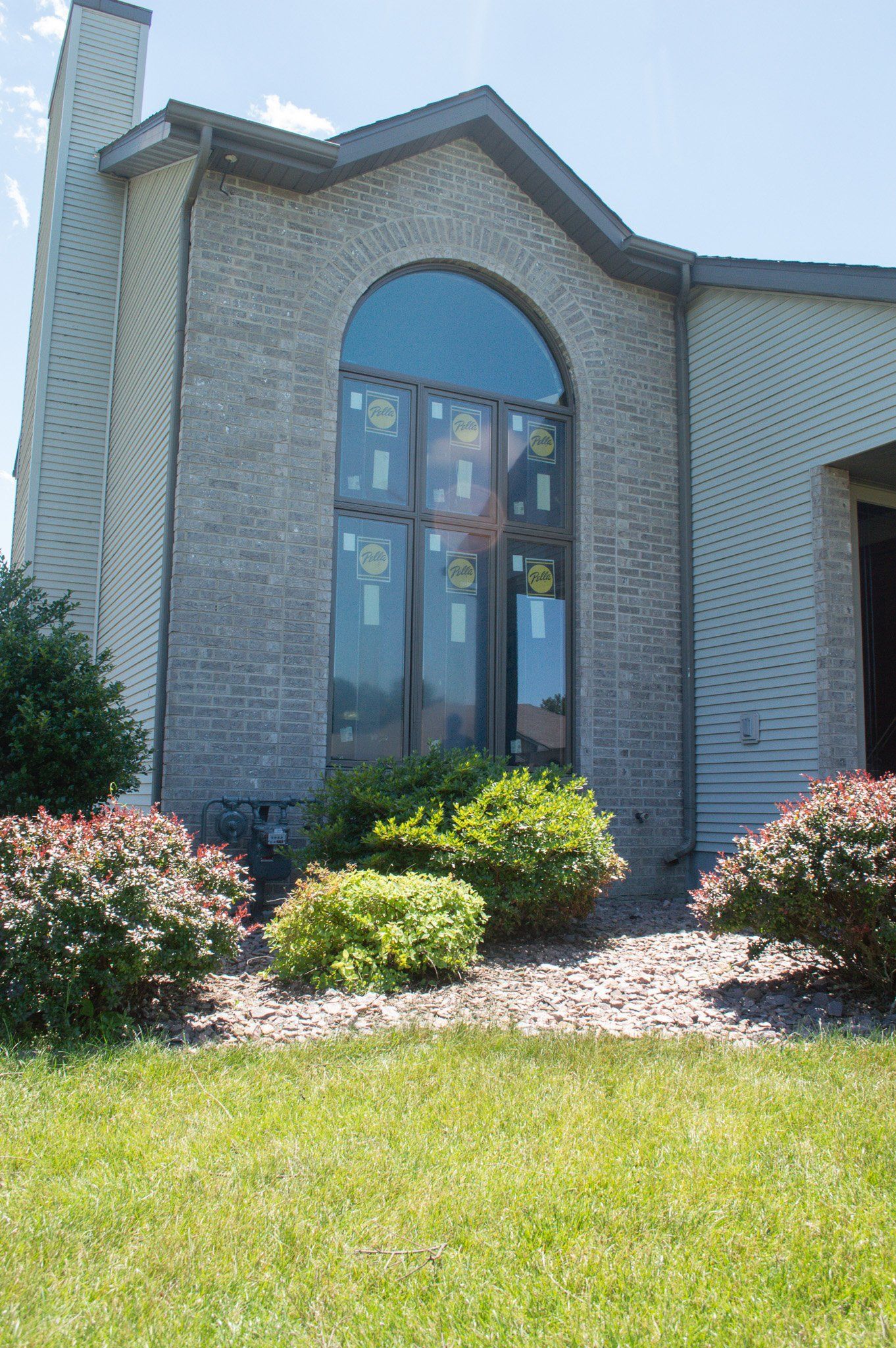 Brick house exterior with arched window, trimmed shrubs, and green lawn