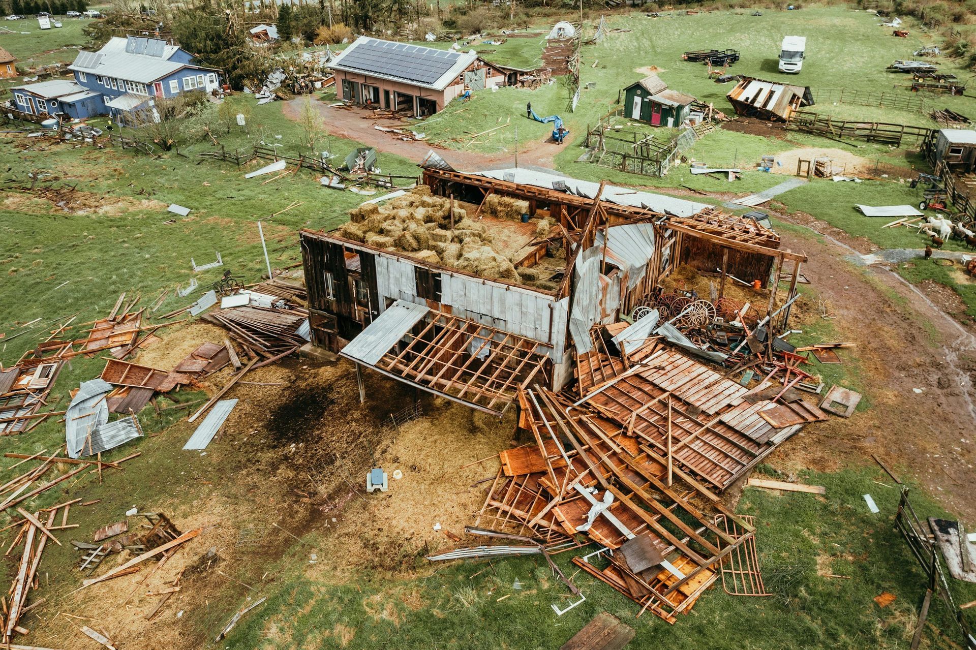 Severely damaged house with collapsed roof and debris scattered across a grassy rural area.