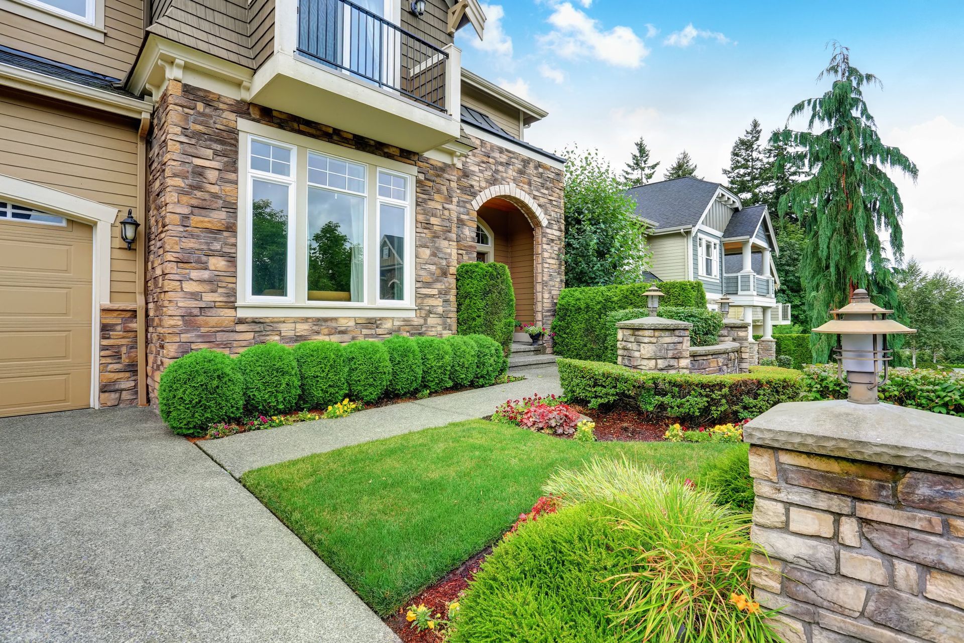 Suburban brick house with manicured front lawn, shrubs, and stone entry pathway