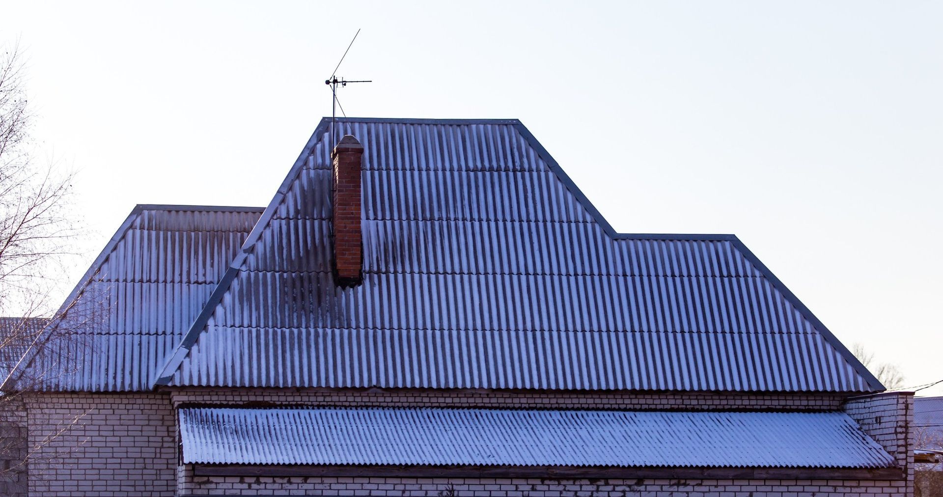 Blue corrugated metal roof with a central chimney and small weather vane against a pale sky