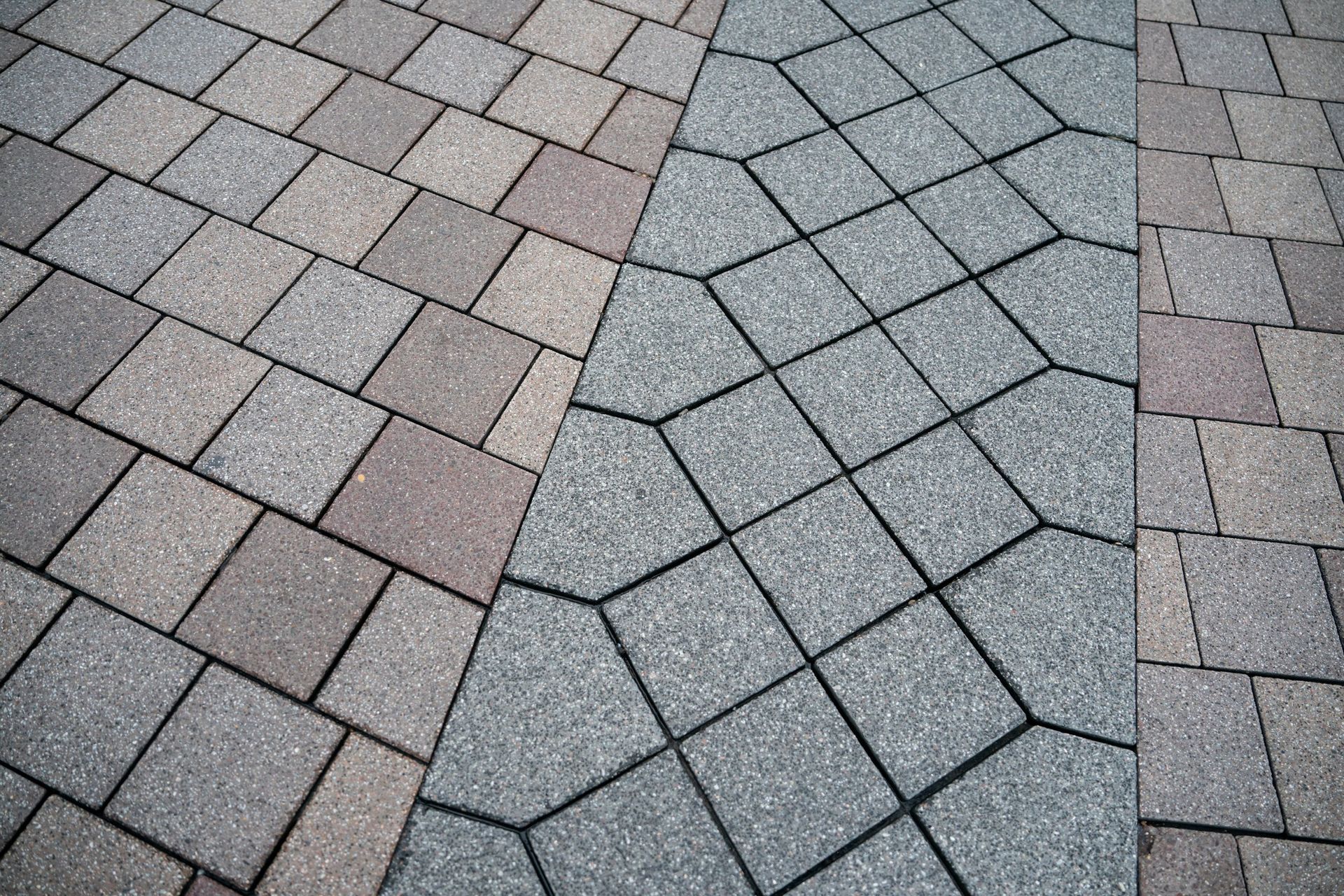 Paved walkway with gray and pink interlocking tiles, divided by a diagonal band of darker stones