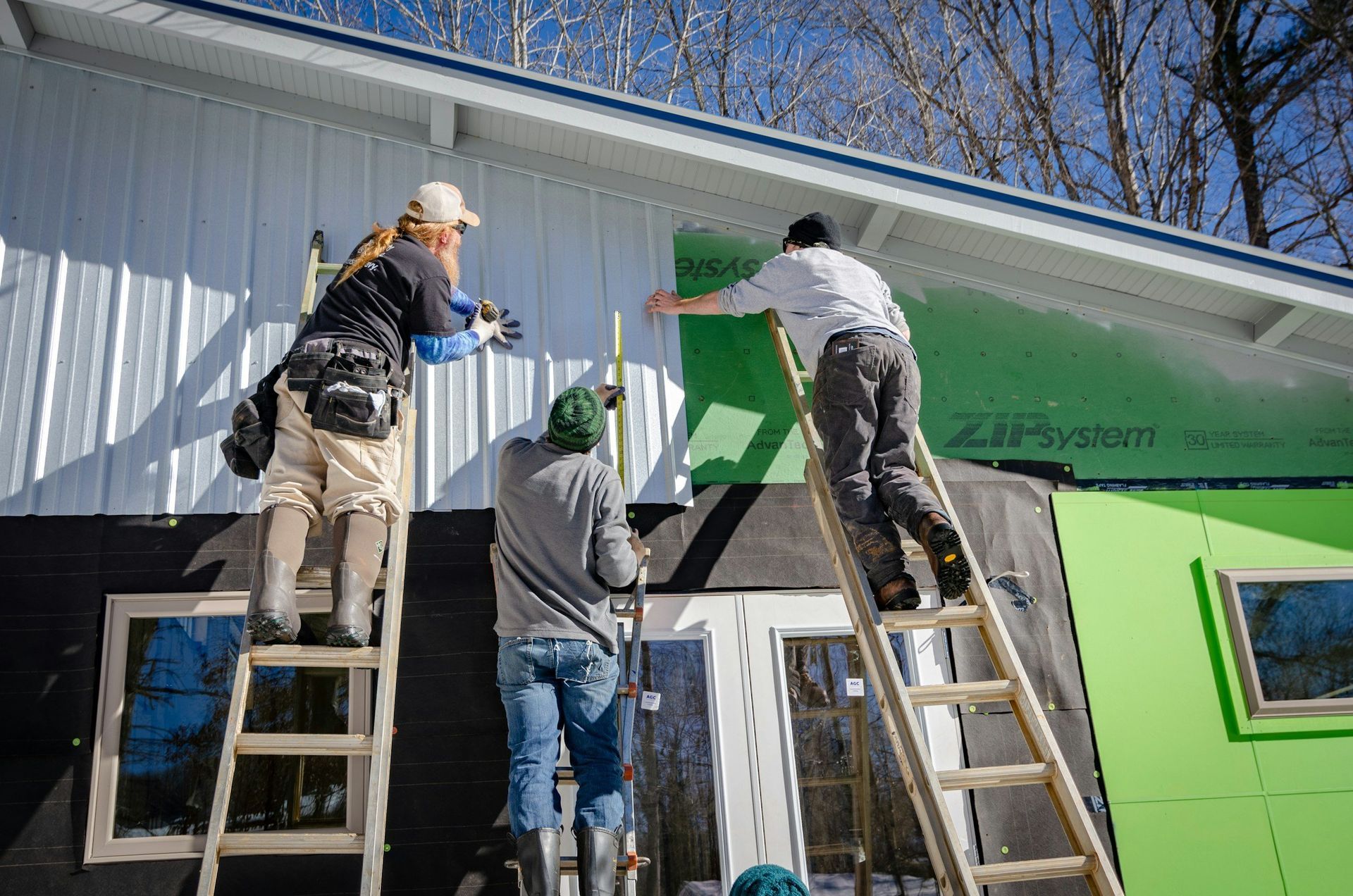 Three workers on ladders painting a white and green building exterior