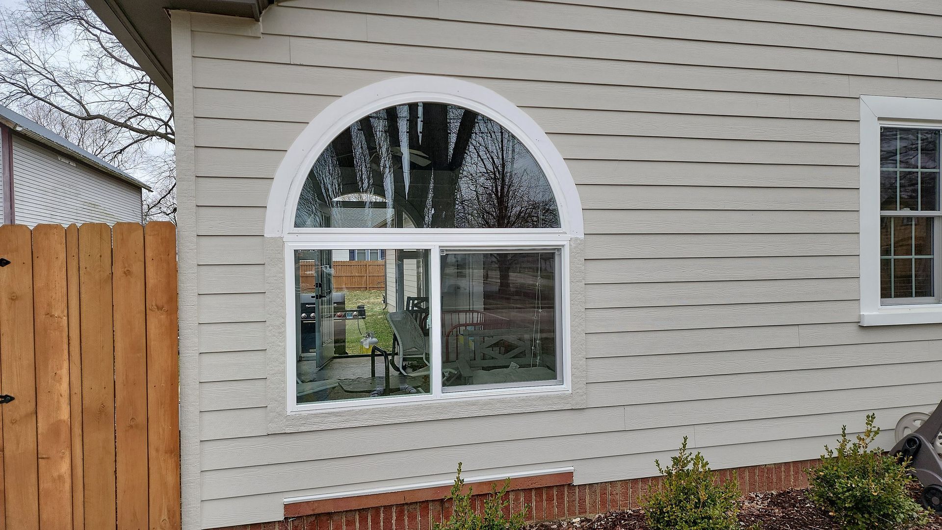 House exterior with white siding, arched window, and wooden fence beside a garden bed
