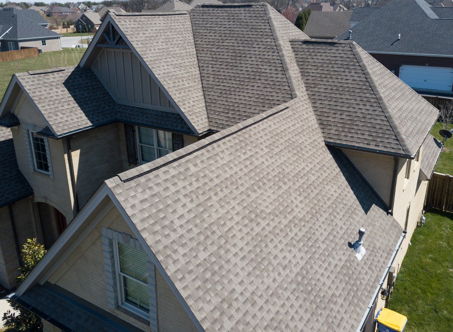 Aerial view of a house with multiple gray shingled roof sections and dormer windows