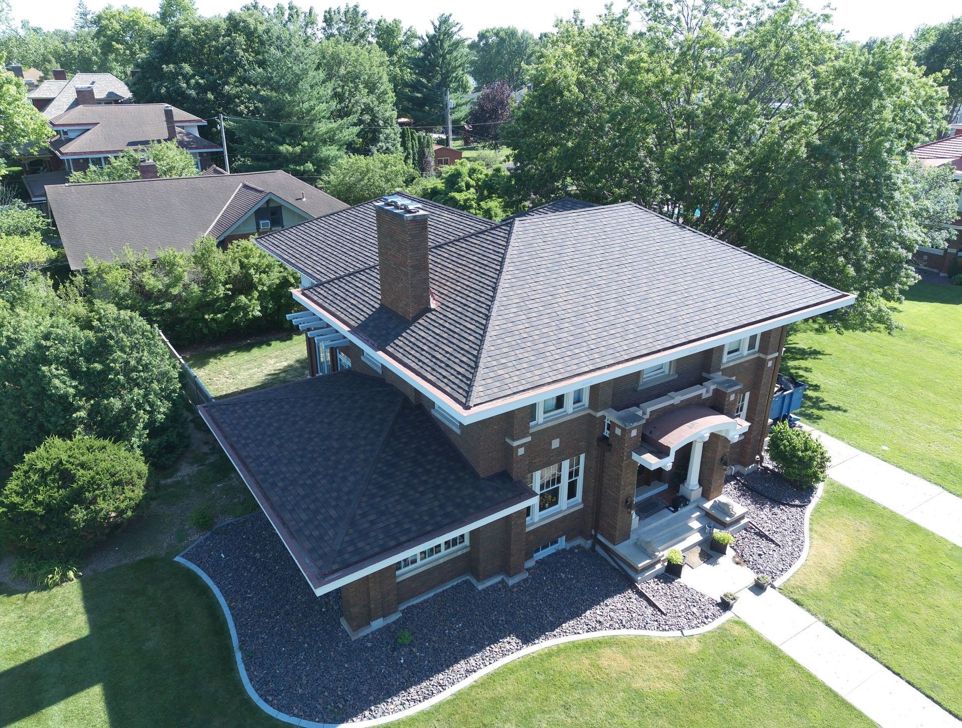 Aerial view of a brick house with a dark roof, surrounded by green trees and lawn.