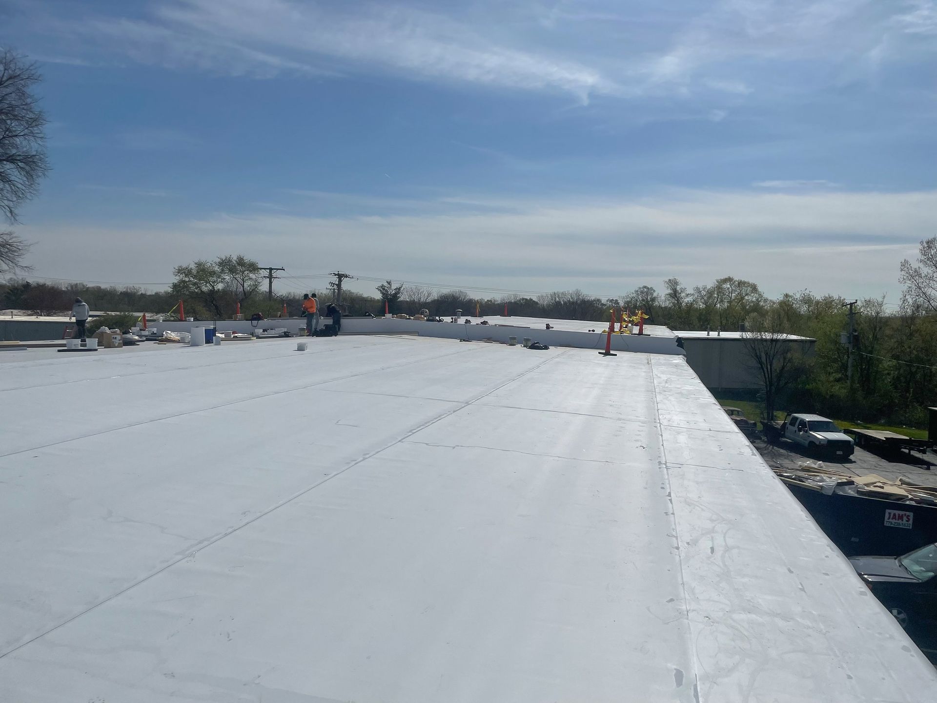 White rooftop under blue sky with distant workers and trees on the horizon