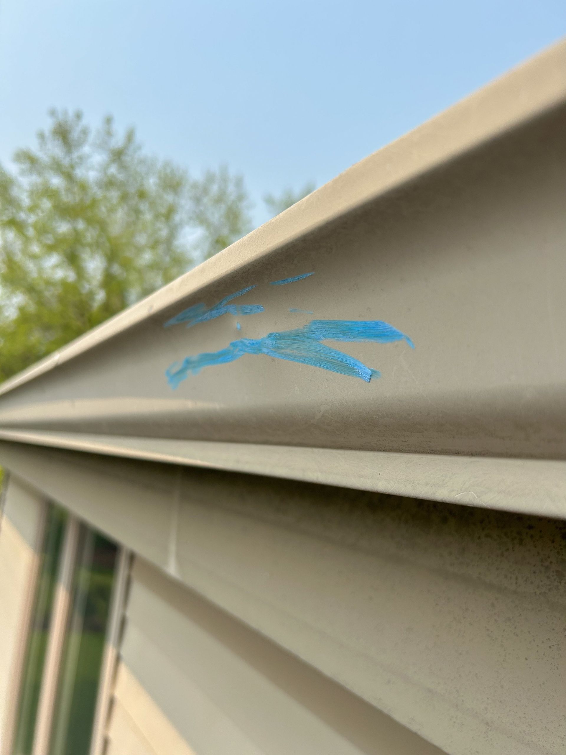 Close-up of beige vinyl siding with blue chalk marks near the roof edge outdoors