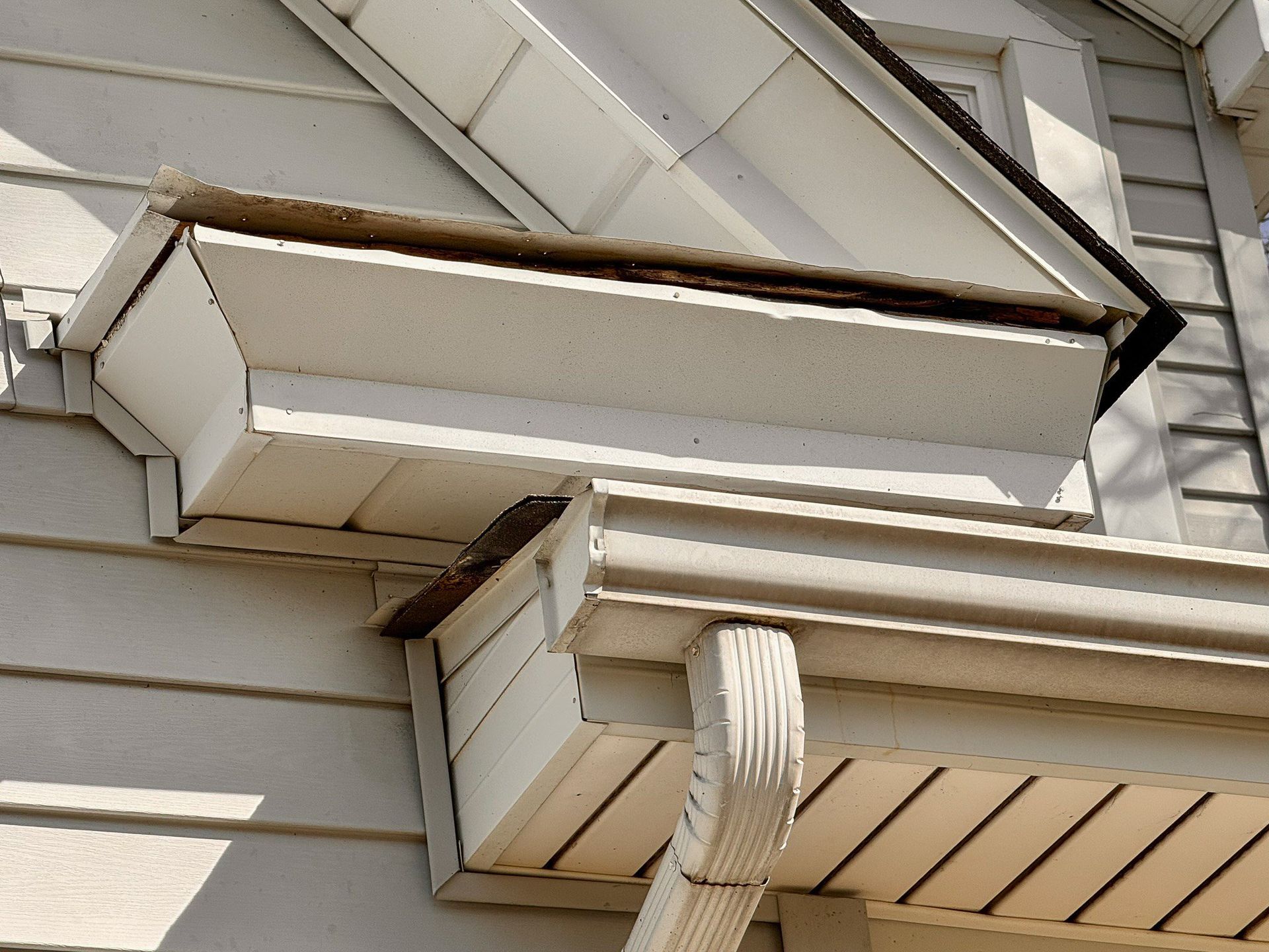 White house roof eaves and soffit detail beneath beige siding, viewed from below