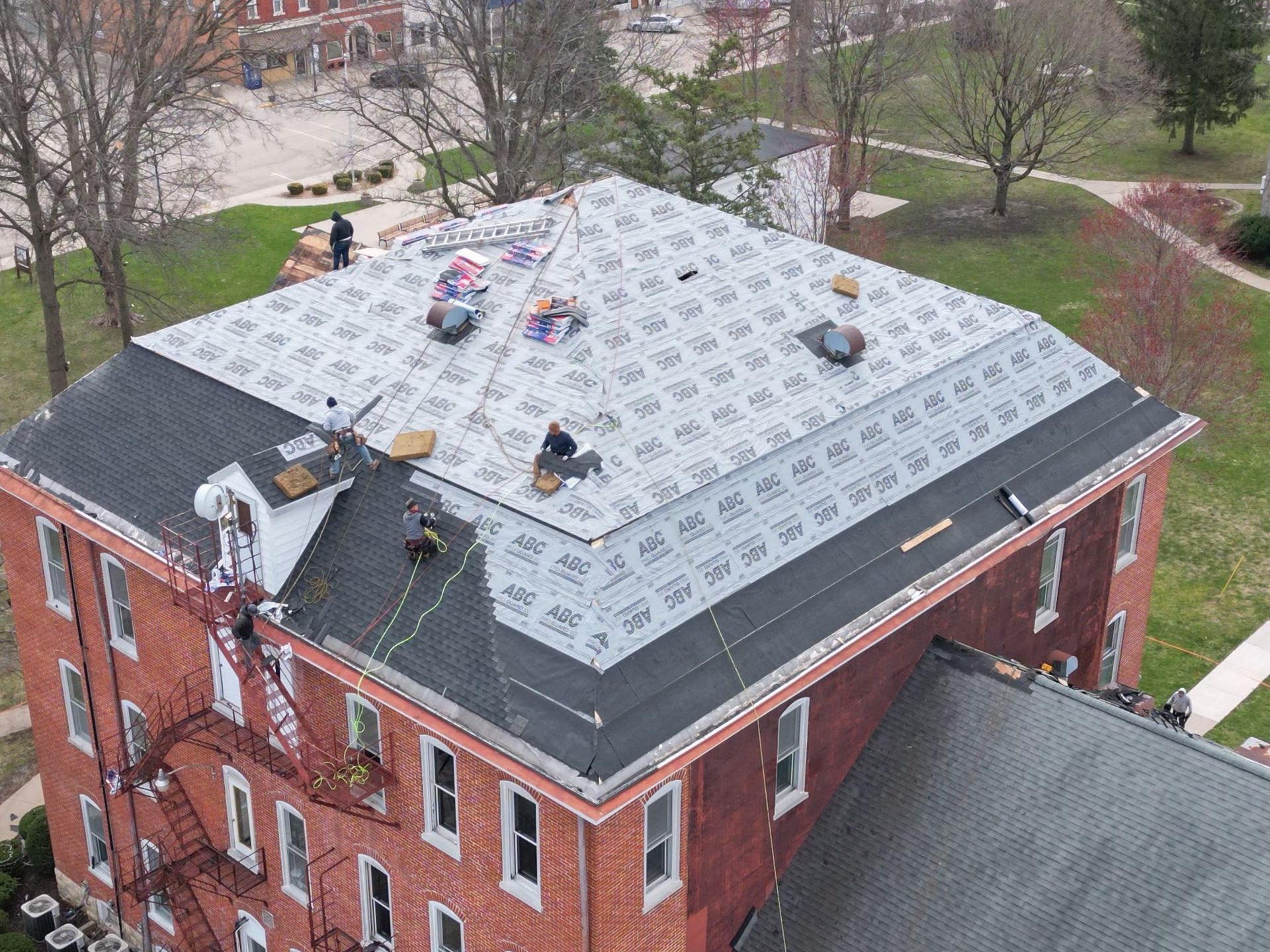 Aerial view of a red brick building roof with workers and a dark gray roof under repair