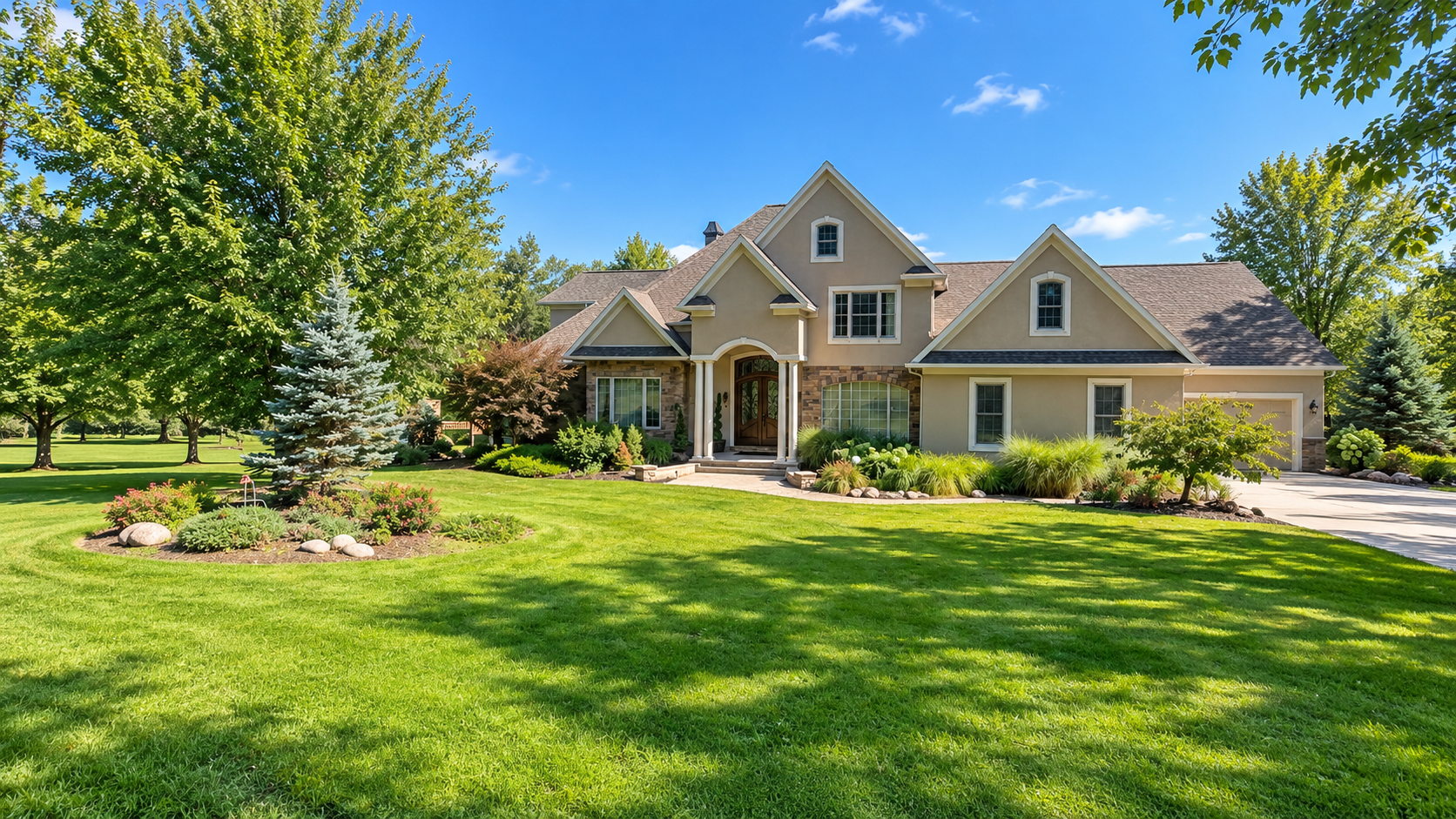 Suburban beige house with a manicured green lawn and mature trees on a sunny day