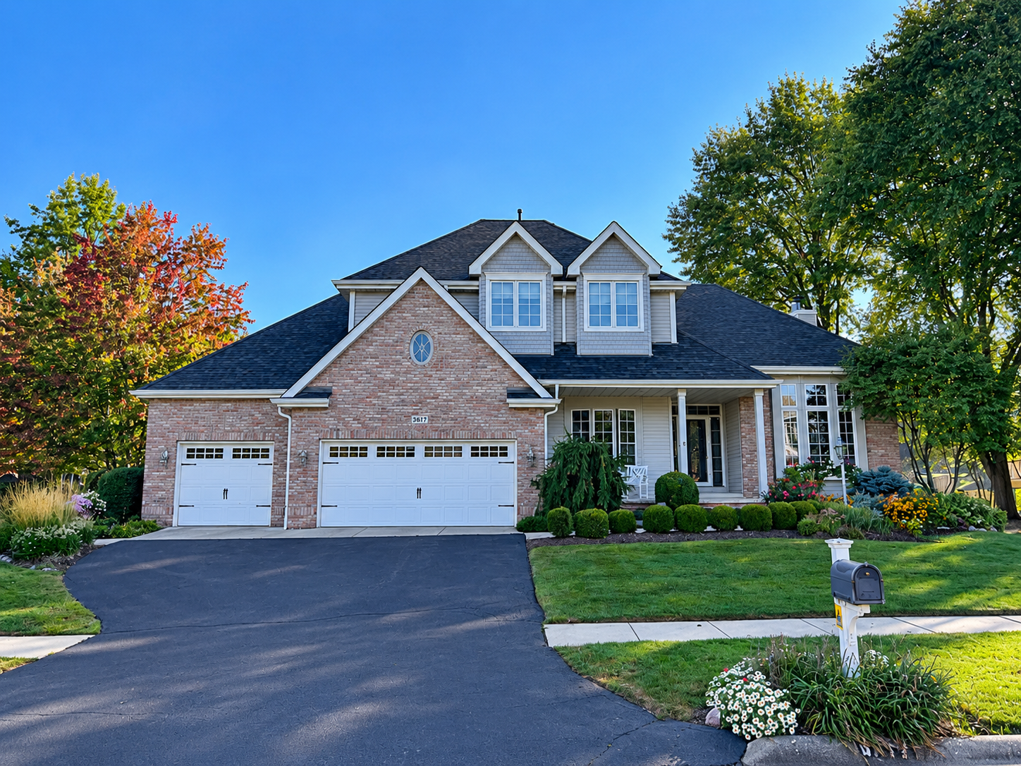 Suburban brick house with three-car garage, blue roof, and manicured lawn on a sunny day