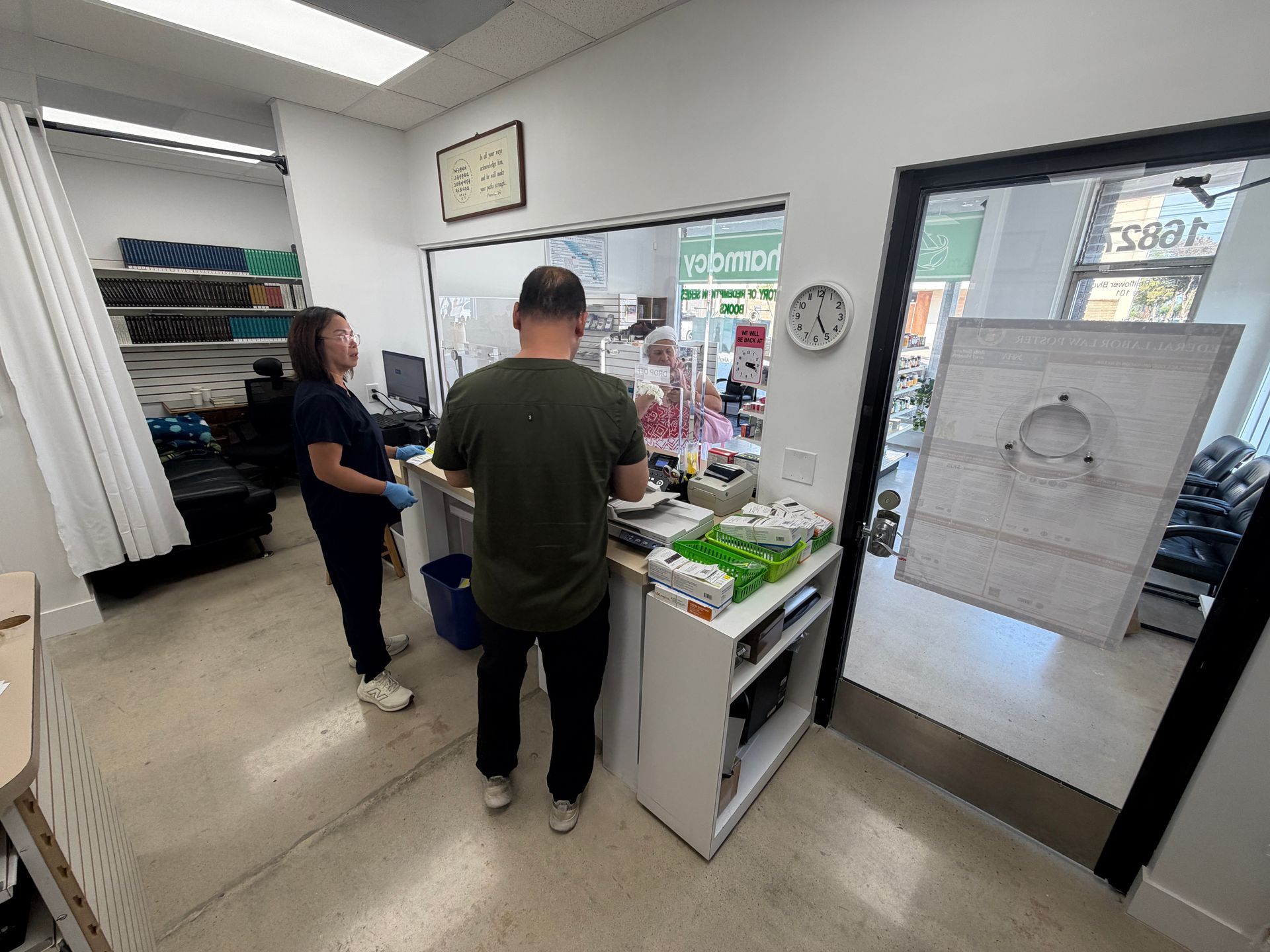 Two people at a checkout counter in a small shop, with shelves and a door in the background.