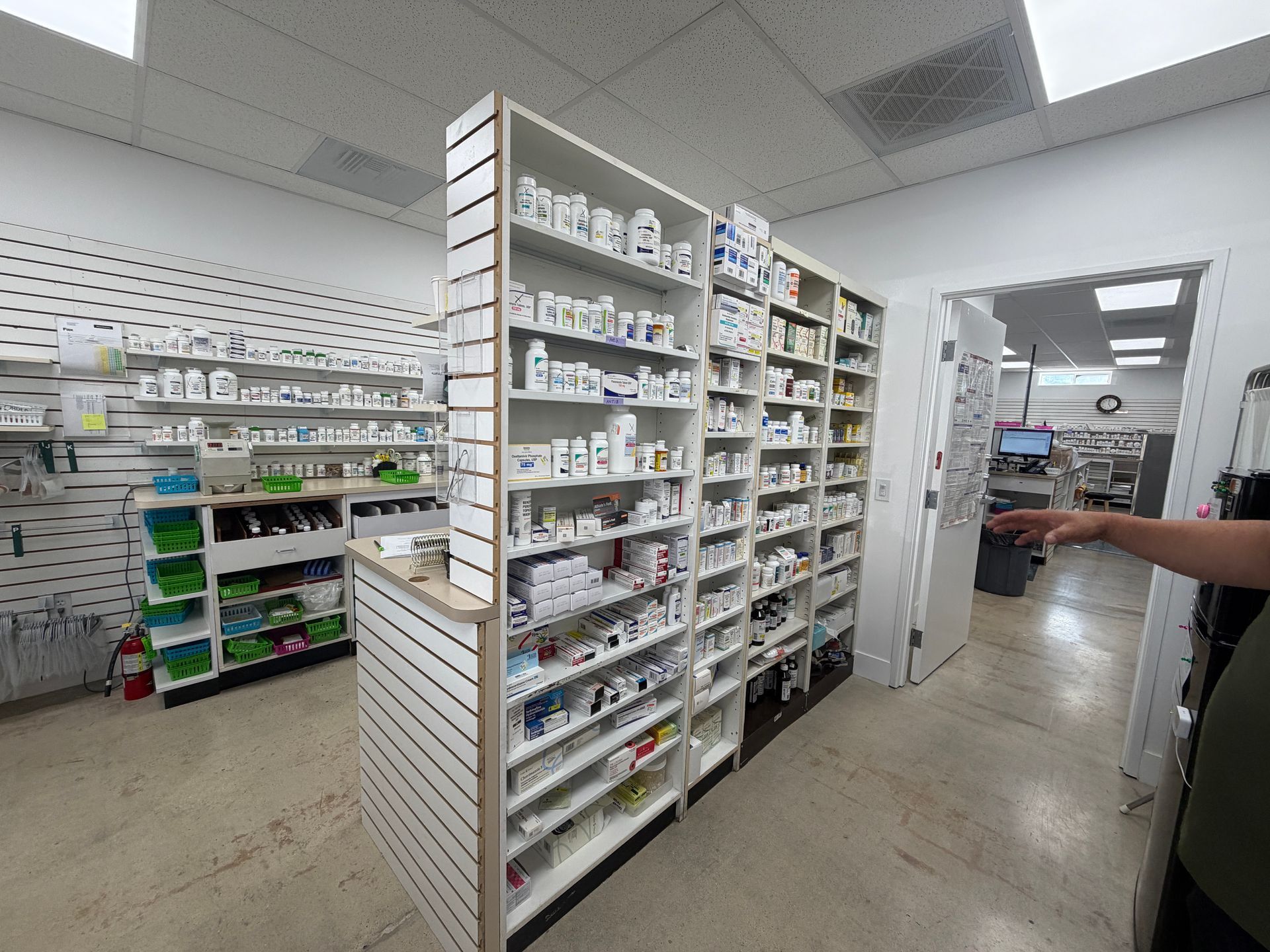 Pharmacy aisle with shelves of medications and a person pointing toward the back area