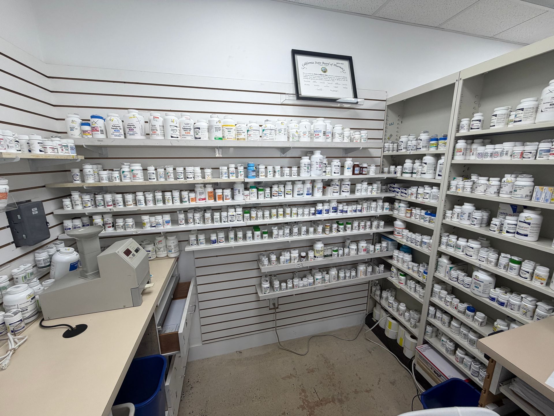Small pharmacy stockroom with shelves of labeled medicine bottles and supplies, no people visible