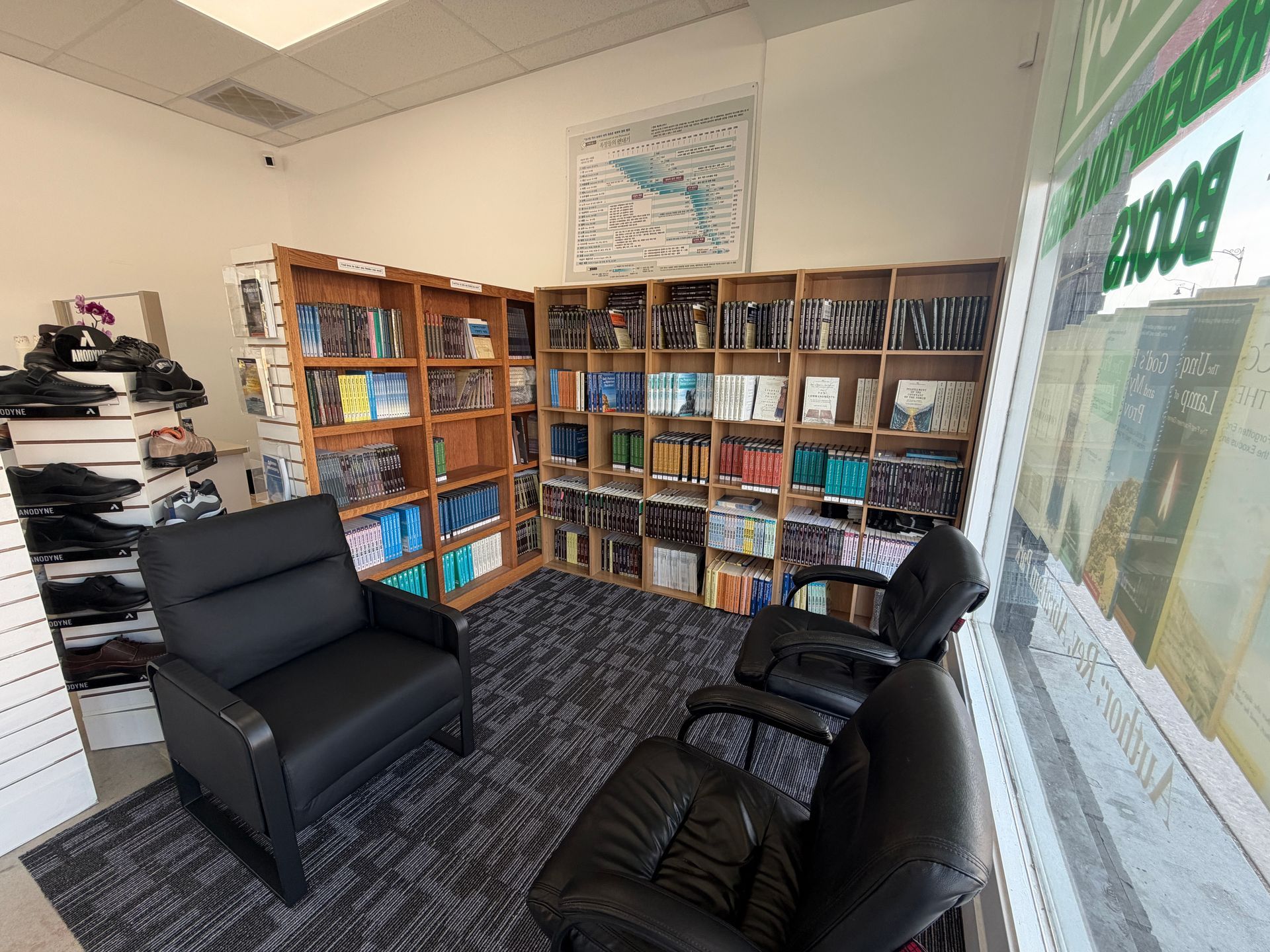 Small library room with black chairs, wooden bookshelves, and a large window.