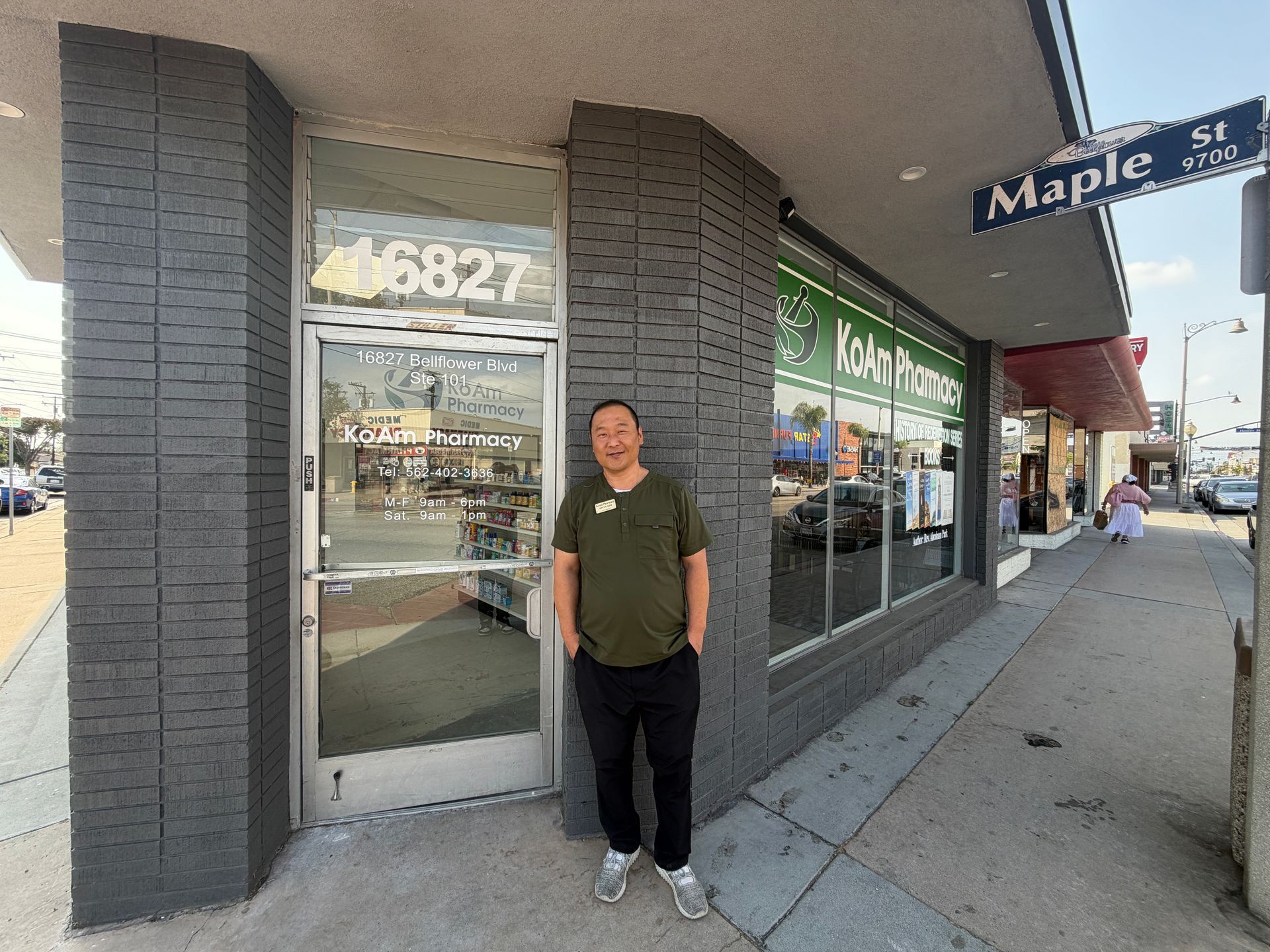 Person standing outside a storefront on a sidewalk corner under the Maple St sign.