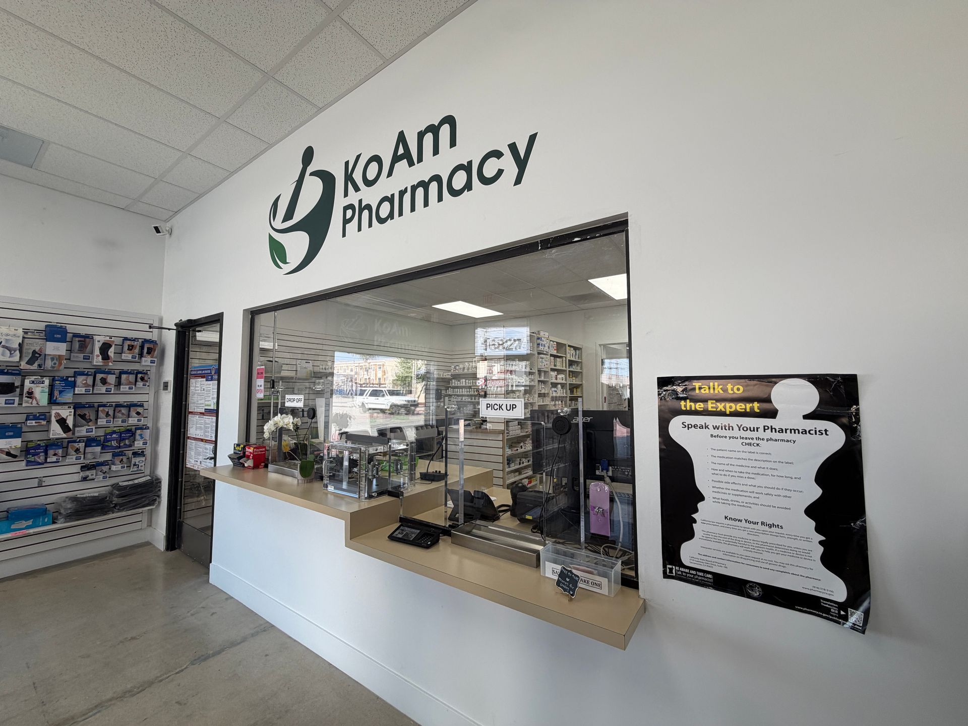 KoAM Pharmacy storefront with service counter, shelves, and black wall sign inside a bright store