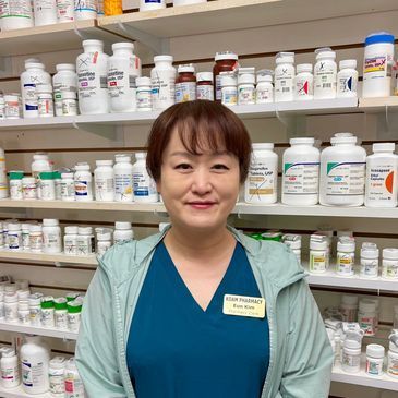 Woman standing in a pharmacy aisle with shelves of medicine bottles behind her