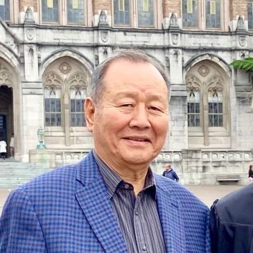 Smiling man in a blue checkered jacket standing before a historic stone building