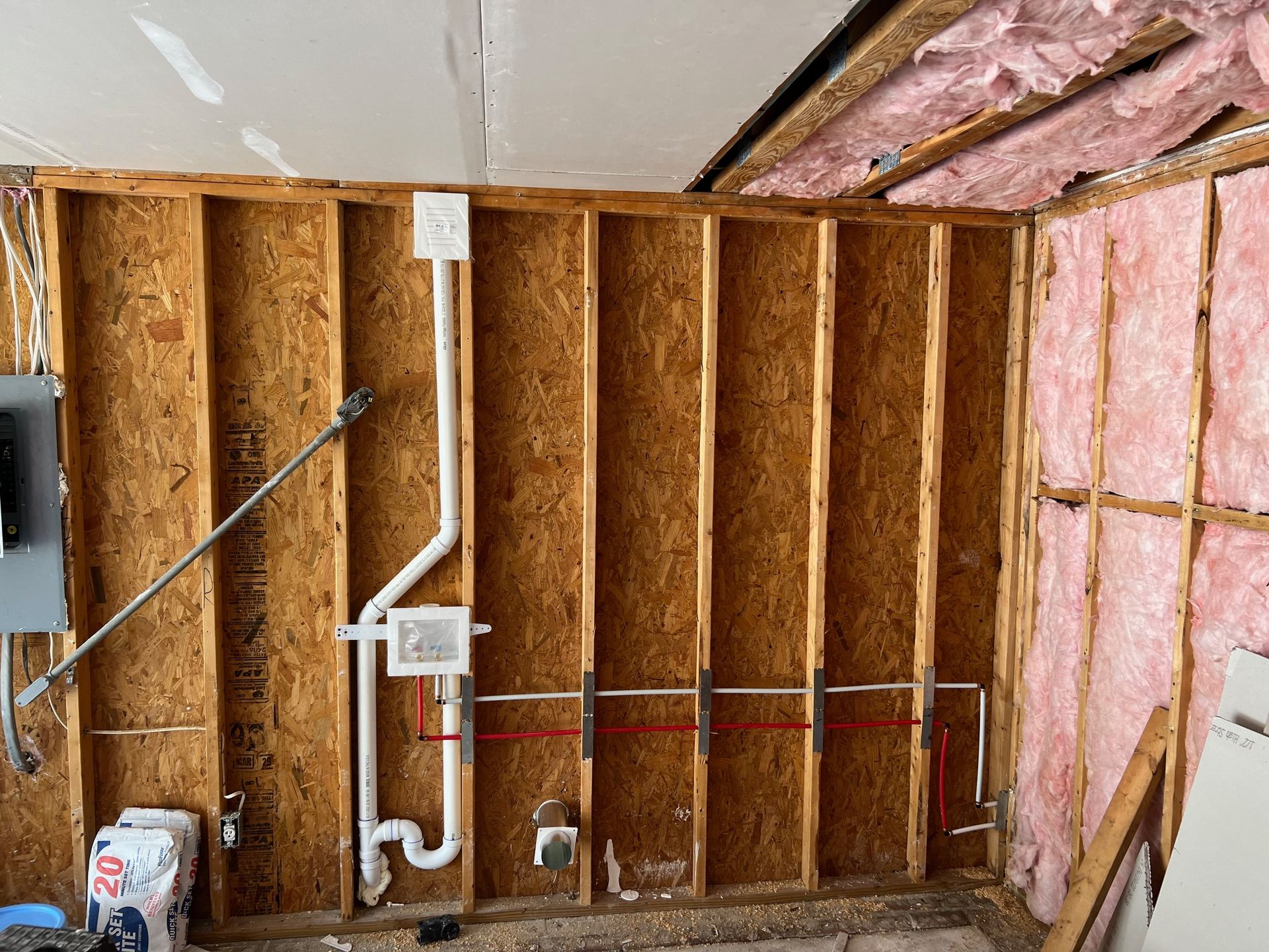 Interior view of a partially framed wall with electrical and plumbing installed. Pink insulation visible.