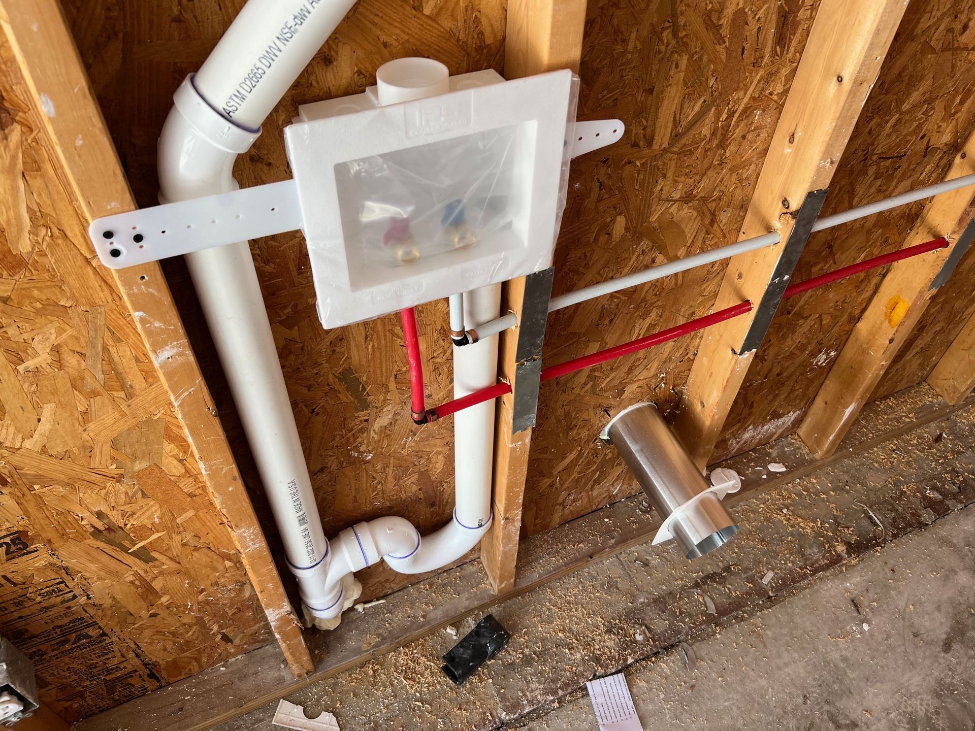 White laundry box with plumbing installed on a wood wall. Red and white pipes are visible.