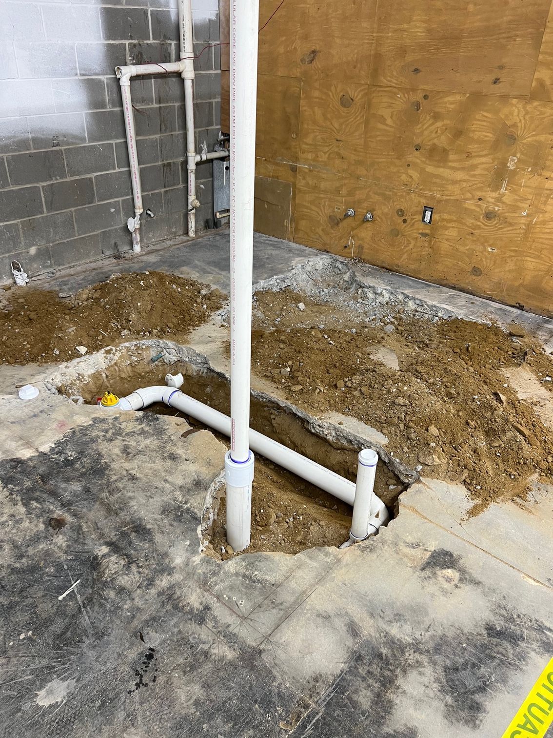 Construction site with exposed plumbing pipes in concrete floor. Dirt piles around excavated areas.