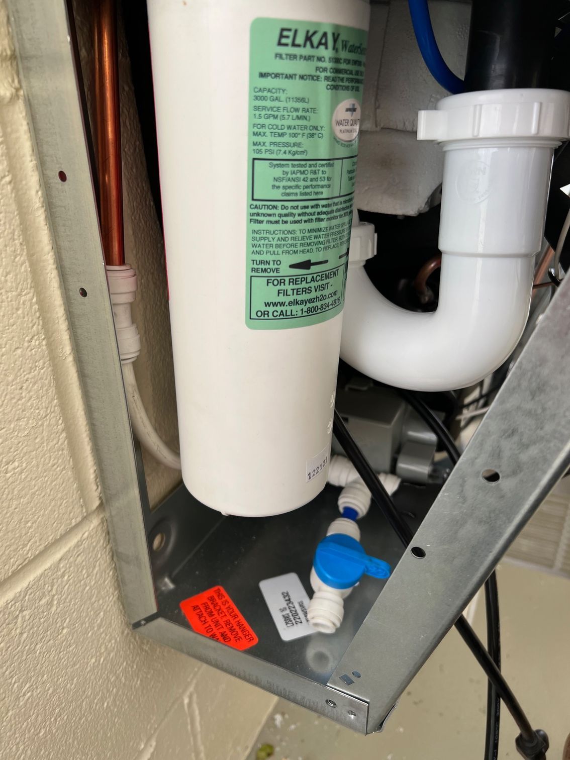 Water filter system installed under a sink. White filter, pipes, and shut-off valve within a metal frame.