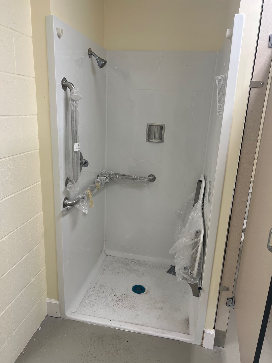 Accessible shower stall with grab bars and showerhead. White walls, light floor, and neutral color.